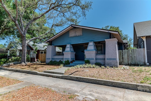 bungalow-style home with fence, covered porch, and brick siding