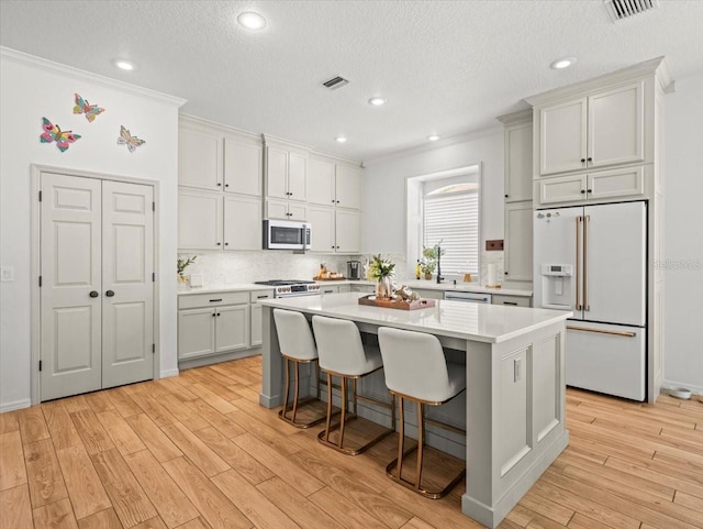kitchen with light countertops, ornamental molding, high end white fridge, a center island, and light wood-type flooring