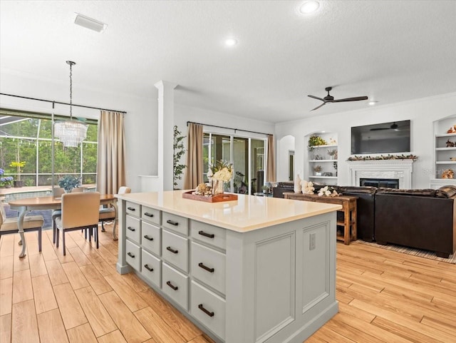 kitchen with a textured ceiling, light wood-style floors, a kitchen island, a fireplace, and a ceiling fan