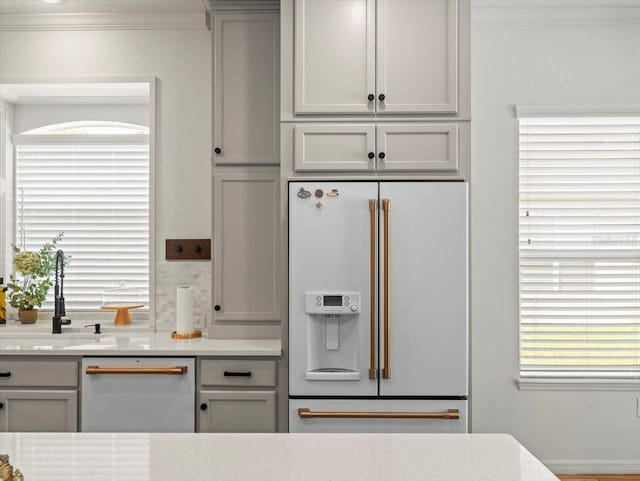 kitchen with a sink, crown molding, white fridge with ice dispenser, dishwashing machine, and gray cabinetry