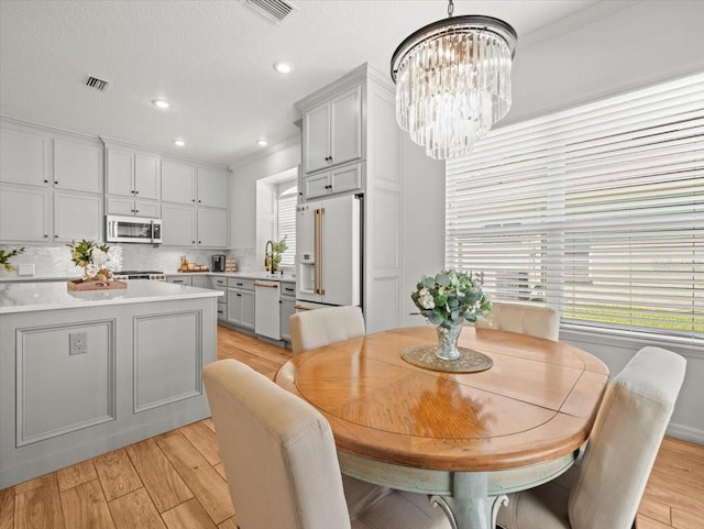 dining space with light wood-type flooring, an inviting chandelier, a healthy amount of sunlight, and visible vents
