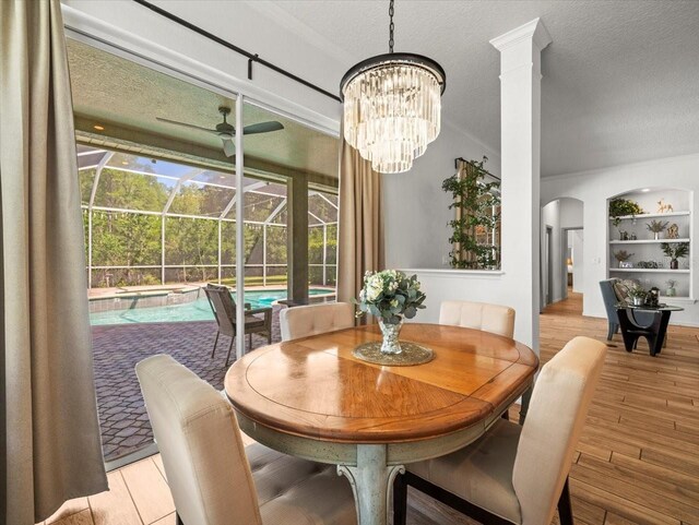 dining area with a textured ceiling, arched walkways, a sunroom, and ceiling fan with notable chandelier