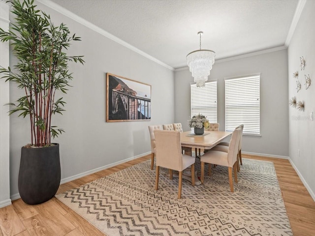 dining room featuring a chandelier, light wood-type flooring, crown molding, baseboards, and a textured ceiling