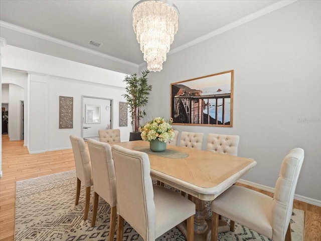 dining area featuring crown molding, visible vents, arched walkways, an inviting chandelier, and light wood finished floors