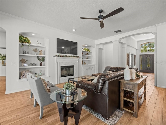 living room featuring a ceiling fan, ornamental molding, arched walkways, and built in shelves