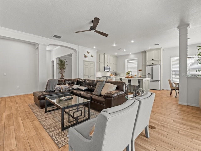 living room with visible vents, ornate columns, a ceiling fan, and light wood-style floors