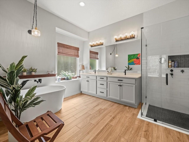 full bath with wood finished floors, a shower stall, double vanity, a sink, and a soaking tub
