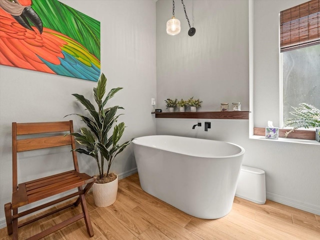 bathroom featuring wood finished floors, a soaking tub, and baseboards