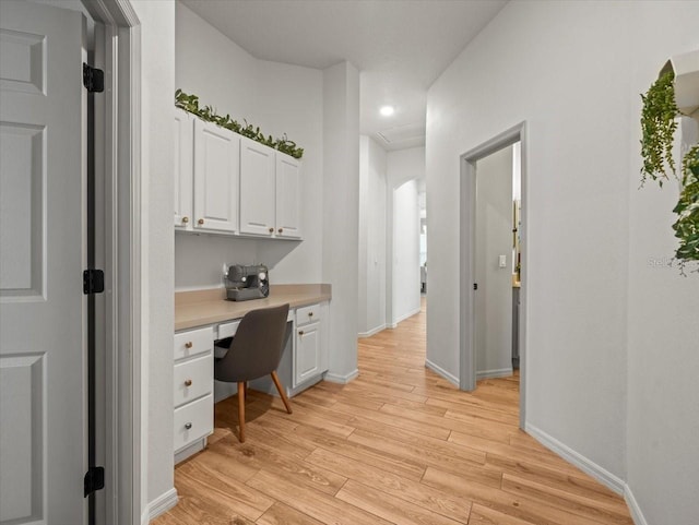office area featuring built in desk, arched walkways, and light wood-style floors
