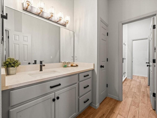 bathroom with baseboards, wood finished floors, a shower stall, and vanity