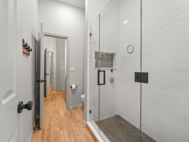 full bath featuring toilet, a stall shower, wood finished floors, and baseboards