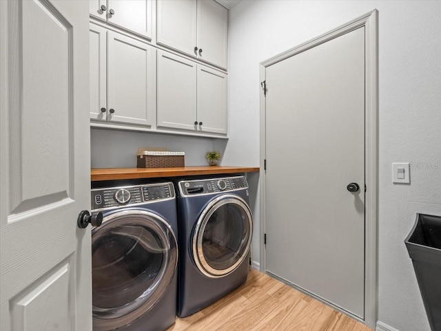 clothes washing area with washer and dryer, cabinet space, and light wood-style floors
