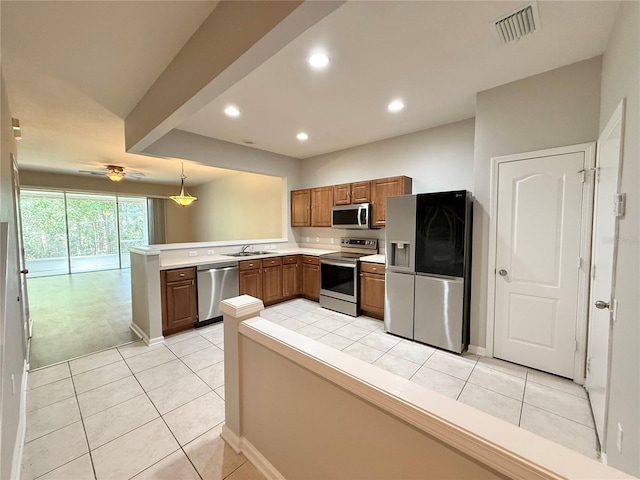 26514 Chimney Spire Ln, Wesley Chapel, FL 33544 - kitchen with stainless steel appliances, a peninsula, a sink, brown cabinetry, and light tile patterned floors