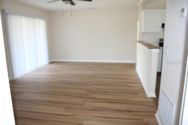 unfurnished room with ceiling fan, light wood-type flooring, visible vents, and baseboards