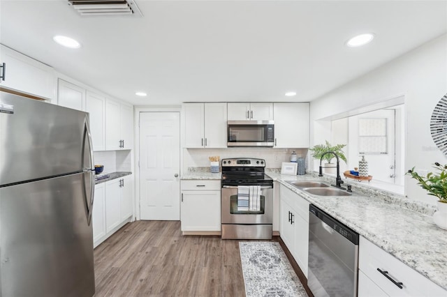 kitchen featuring visible vents, appliances with stainless steel finishes, light wood-type flooring, a sink, and white cabinets