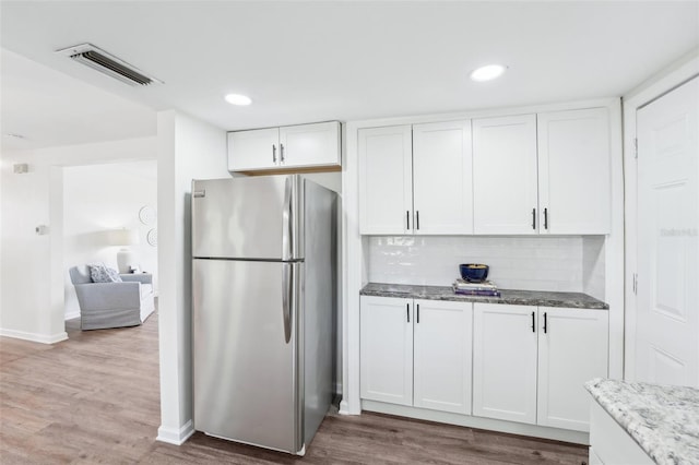 kitchen featuring visible vents, wood finished floors, freestanding refrigerator, stone counters, and white cabinetry
