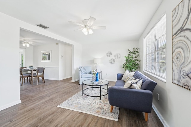 living area featuring visible vents, a ceiling fan, baseboards, and wood finished floors