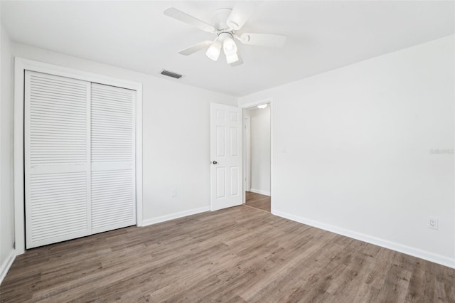 unfurnished bedroom with a ceiling fan, visible vents, wood finished floors, baseboards, and a closet