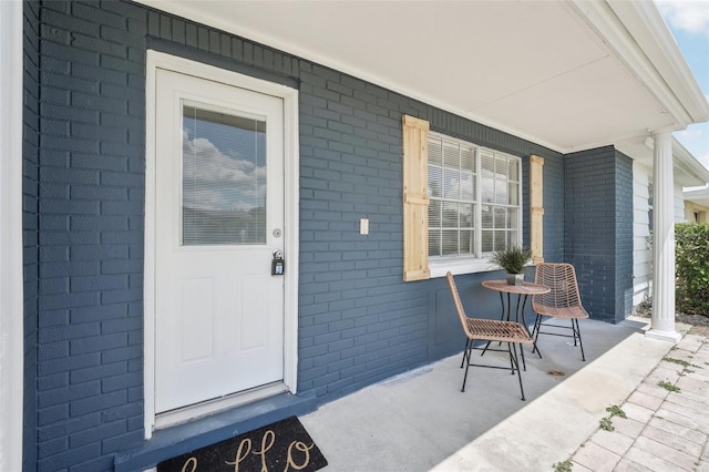 doorway to property featuring a porch and brick siding
