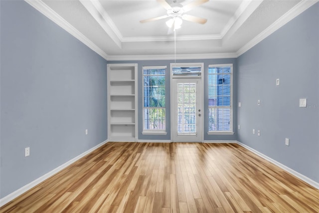 empty room featuring wood finished floors, ornamental molding, ceiling fan, baseboards, and a raised ceiling
