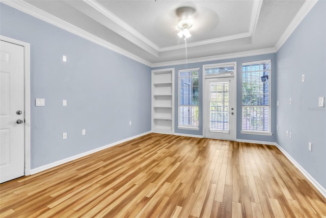 unfurnished room with ornamental molding, a tray ceiling, light wood finished floors, and baseboards