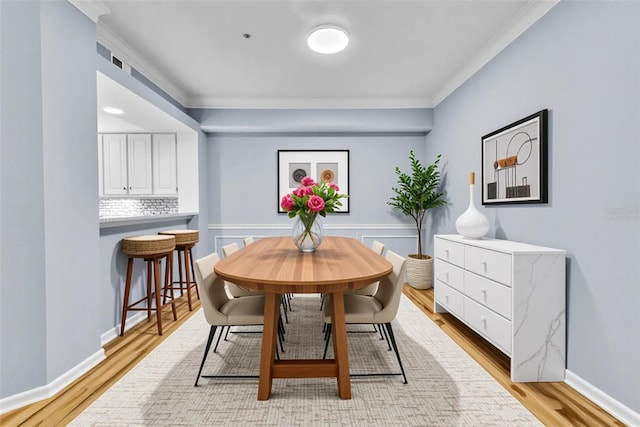 dining space featuring ornamental molding, light wood-style flooring, and baseboards