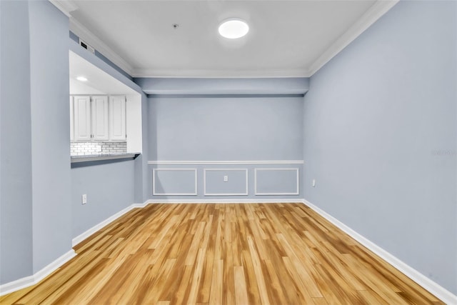 spare room featuring light wood-style floors, baseboards, ornamental molding, and wainscoting