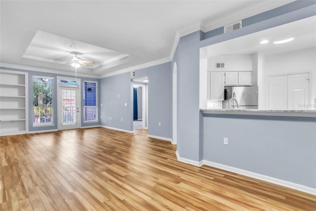unfurnished living room with ornamental molding, light wood-type flooring, ceiling fan, visible vents, and a tray ceiling