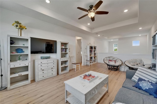 living area featuring a ceiling fan, a tray ceiling, recessed lighting, and light wood-style floors