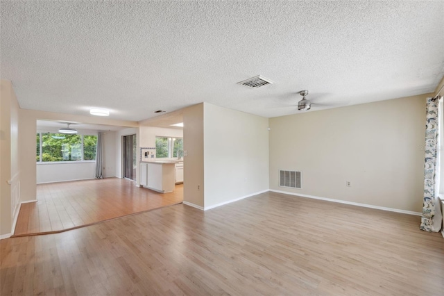 unfurnished living room featuring a ceiling fan, light wood-style flooring, a textured ceiling, and baseboards