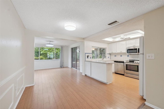kitchen with appliances with stainless steel finishes, light countertops, open floor plan, a textured ceiling, and decorative backsplash