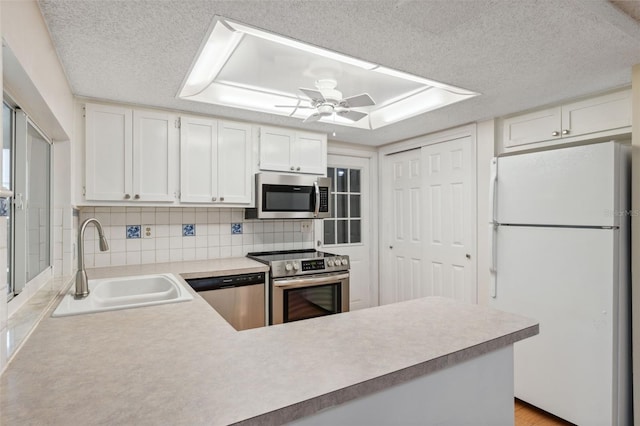kitchen featuring stainless steel appliances, a sink, a peninsula, light countertops, and a textured ceiling