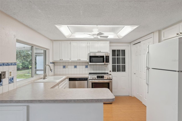 kitchen featuring appliances with stainless steel finishes, a sink, a peninsula, white cabinets, and a textured ceiling