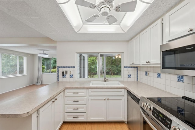 kitchen featuring stainless steel appliances, a sink, a peninsula, ceiling fan, and decorative backsplash