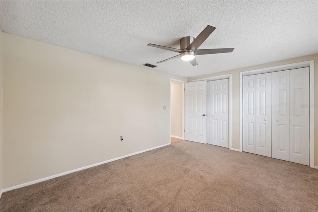 unfurnished bedroom featuring carpet, a textured ceiling, two closets, baseboards, and a ceiling fan