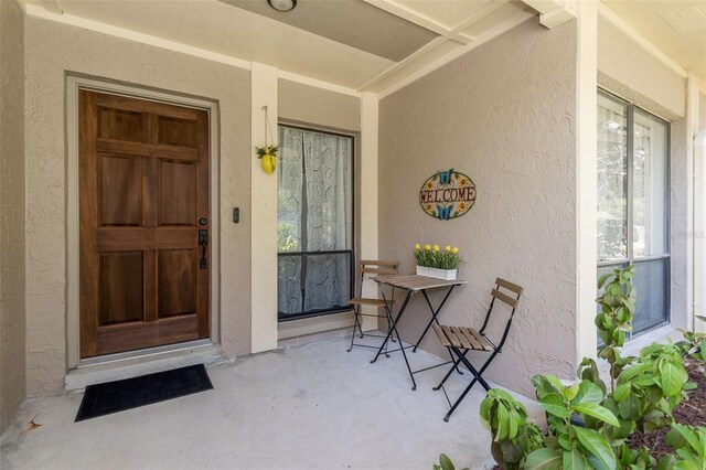 view of exterior entry featuring visible vents, stucco siding, and covered porch
