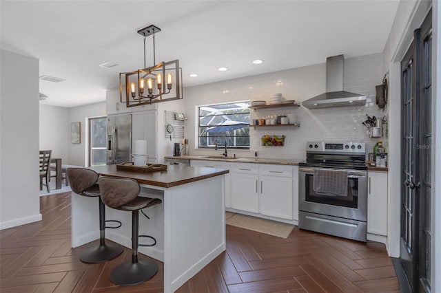 kitchen featuring appliances with stainless steel finishes, a kitchen island, wall chimney range hood, a sink, and white cabinetry