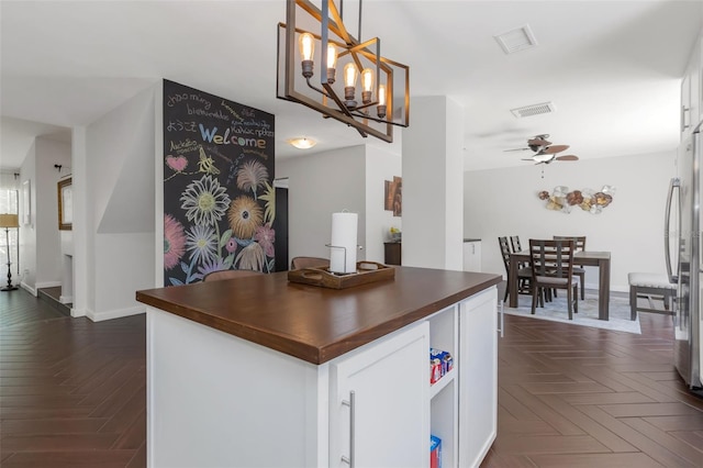kitchen with white cabinetry, visible vents, freestanding refrigerator, and ceiling fan with notable chandelier