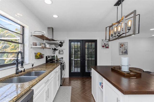 kitchen featuring stainless steel appliances, open shelves, a sink, wall chimney exhaust hood, and french doors