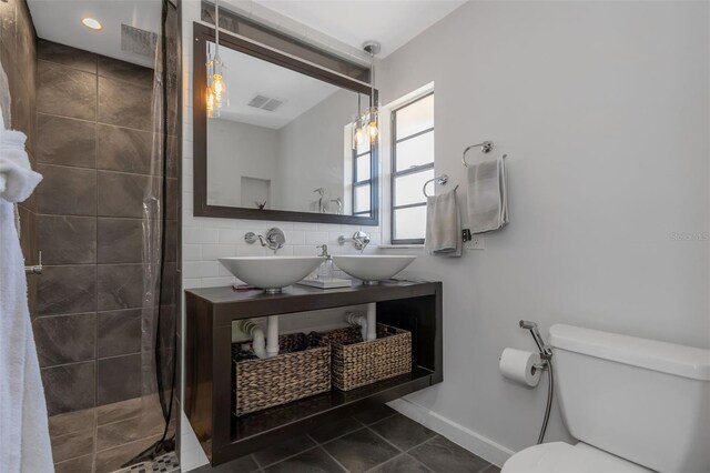 full bath with toilet, a sink, visible vents, and a tile shower
