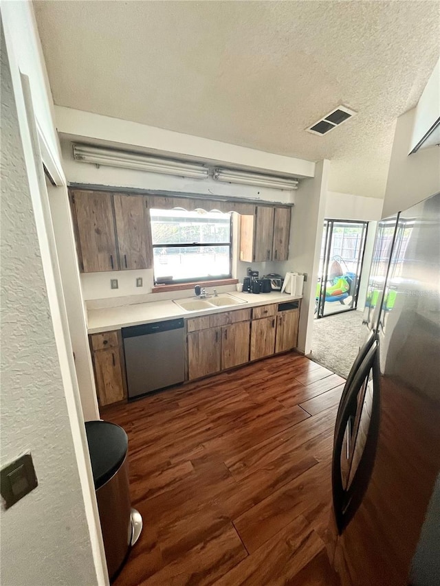 kitchen featuring dark wood finished floors, stainless steel dishwasher, light countertops, a sink, and visible vents