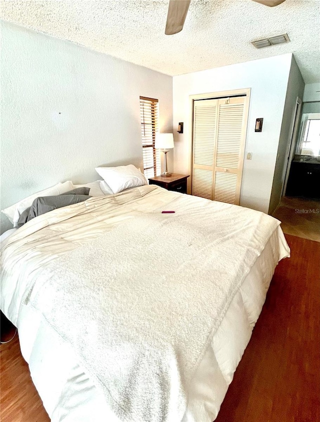 bedroom with a textured ceiling, visible vents, a closet, wood finished floors, and a ceiling fan