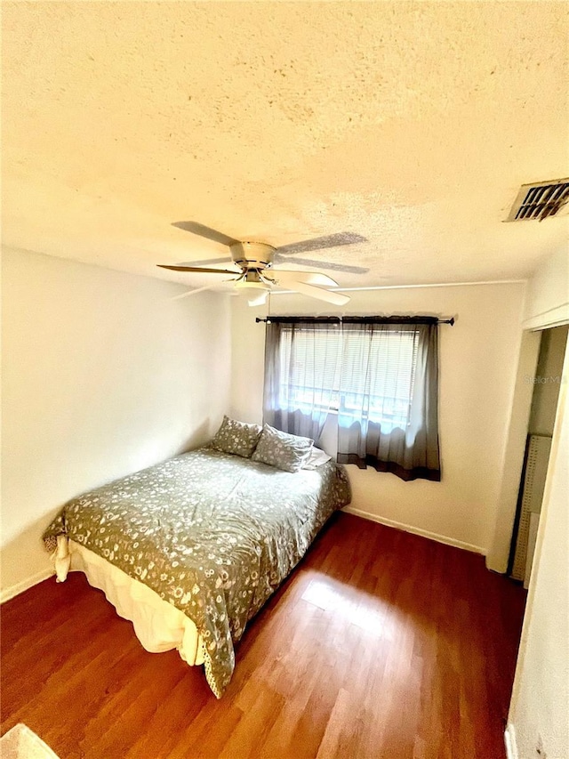 bedroom with a textured ceiling, visible vents, wood finished floors, and baseboards