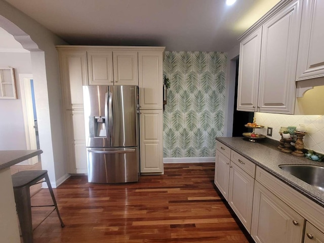 kitchen featuring stainless steel refrigerator with ice dispenser, a sink, baseboards, an accent wall, and wallpapered walls
