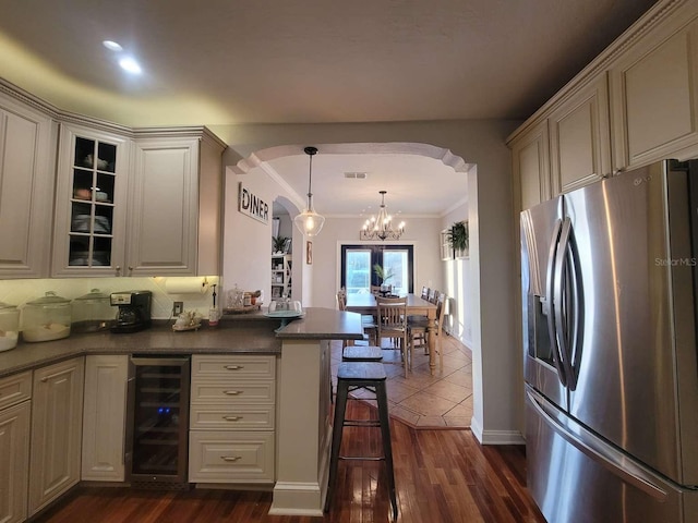 kitchen with dark countertops, stainless steel fridge with ice dispenser, beverage cooler, arched walkways, and a chandelier