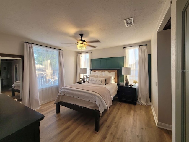 bedroom featuring ceiling fan, a textured ceiling, light wood-style flooring, baseboards, and visible vents