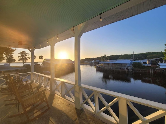 deck at dusk with a water view and a dock