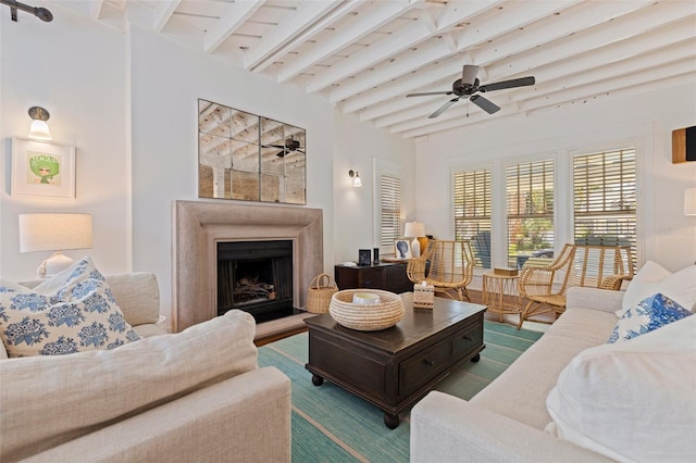 living area featuring beamed ceiling, ceiling fan, and a fireplace with raised hearth