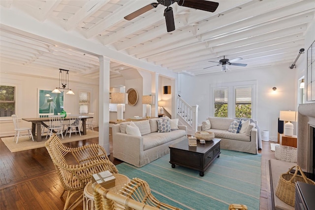 living room with dark wood-type flooring, ceiling fan, stairway, and beamed ceiling