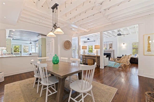 dining space featuring dark wood finished floors, ceiling fan, baseboards, and a fireplace
